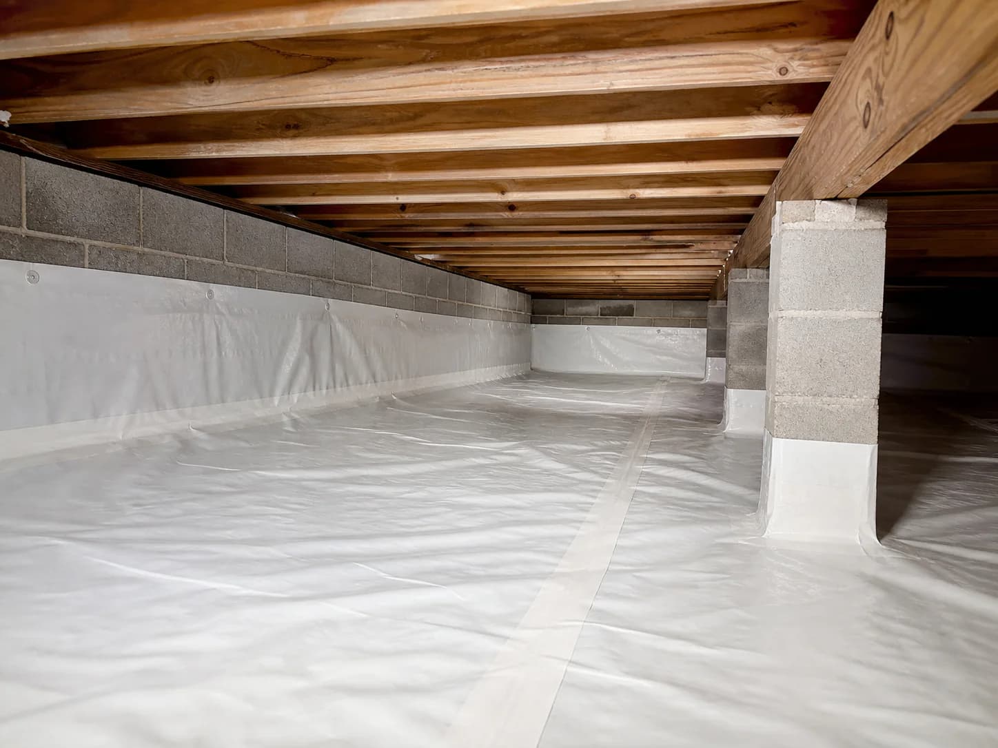 Continuous crawl-space liner at the floor, walls, seams, and support piers beneath a home